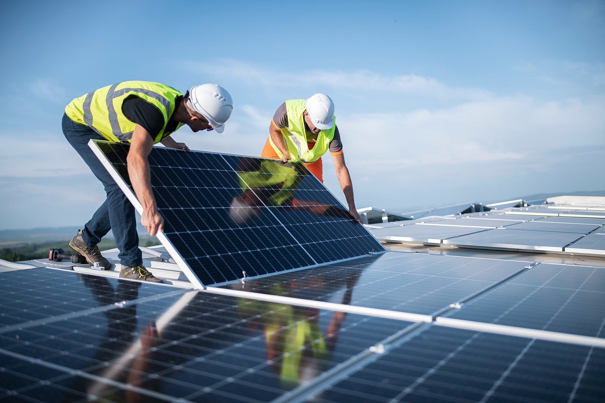 Dois homens com EPIs instalando painéis fotovoltaicos