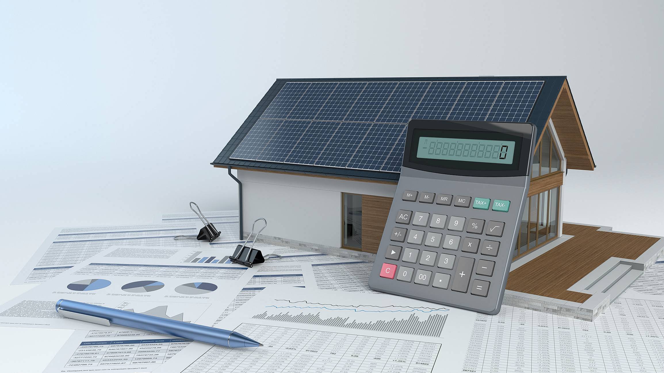 Montagem de uma casa com painéis solares sobre uma mesa com diversos papéis e uma calculadora apoiada sobre a casa