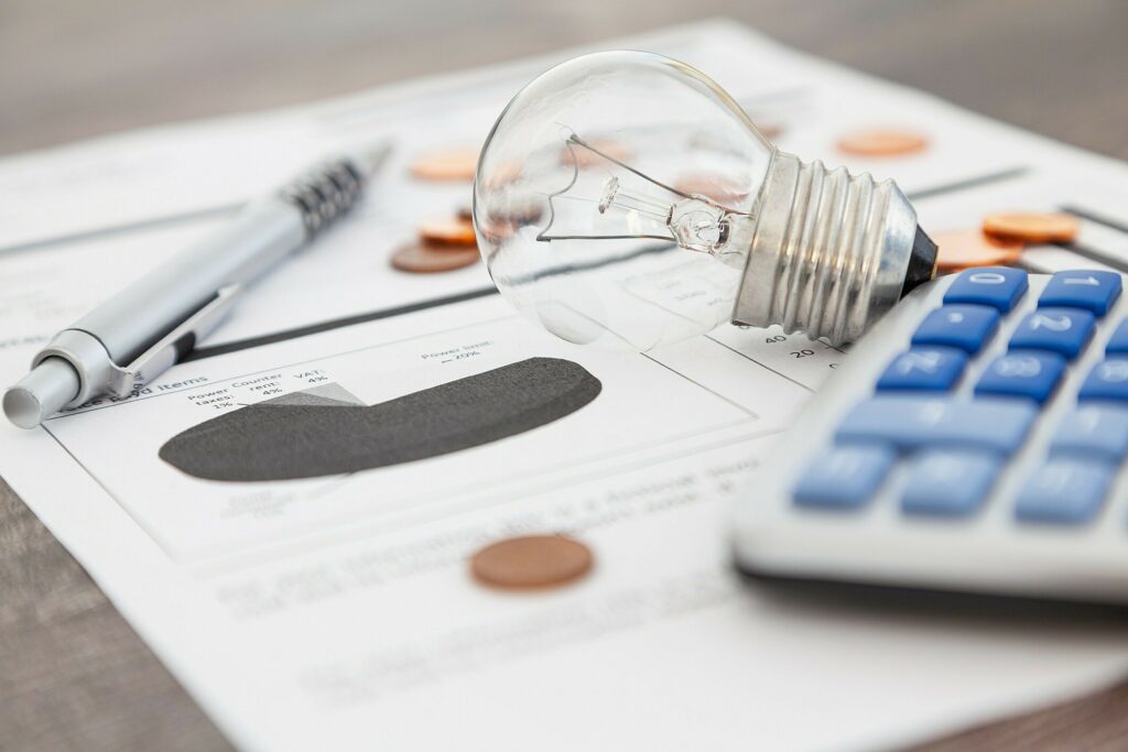 Papel, caneta, calculadora e uma lâmpada sobre uma mesa