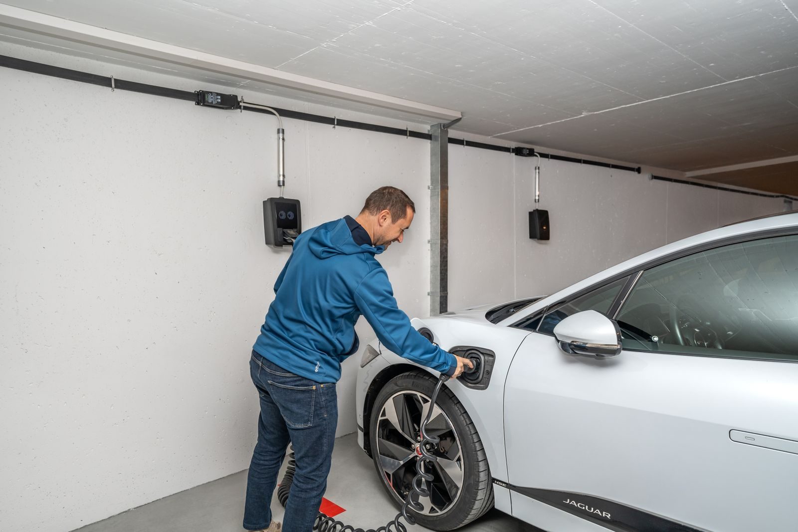 Morador conectando o carro elétrico ao carregador de parede Morador conectando o carro elétrico ao carregador de parede na garagem
