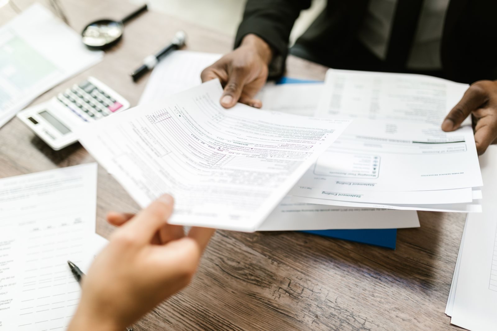 Profissionais comparando propostas impressas sobre uma mesa, Profissionais comparando propostas impressas sobre uma mesa, com calculadora ao lado